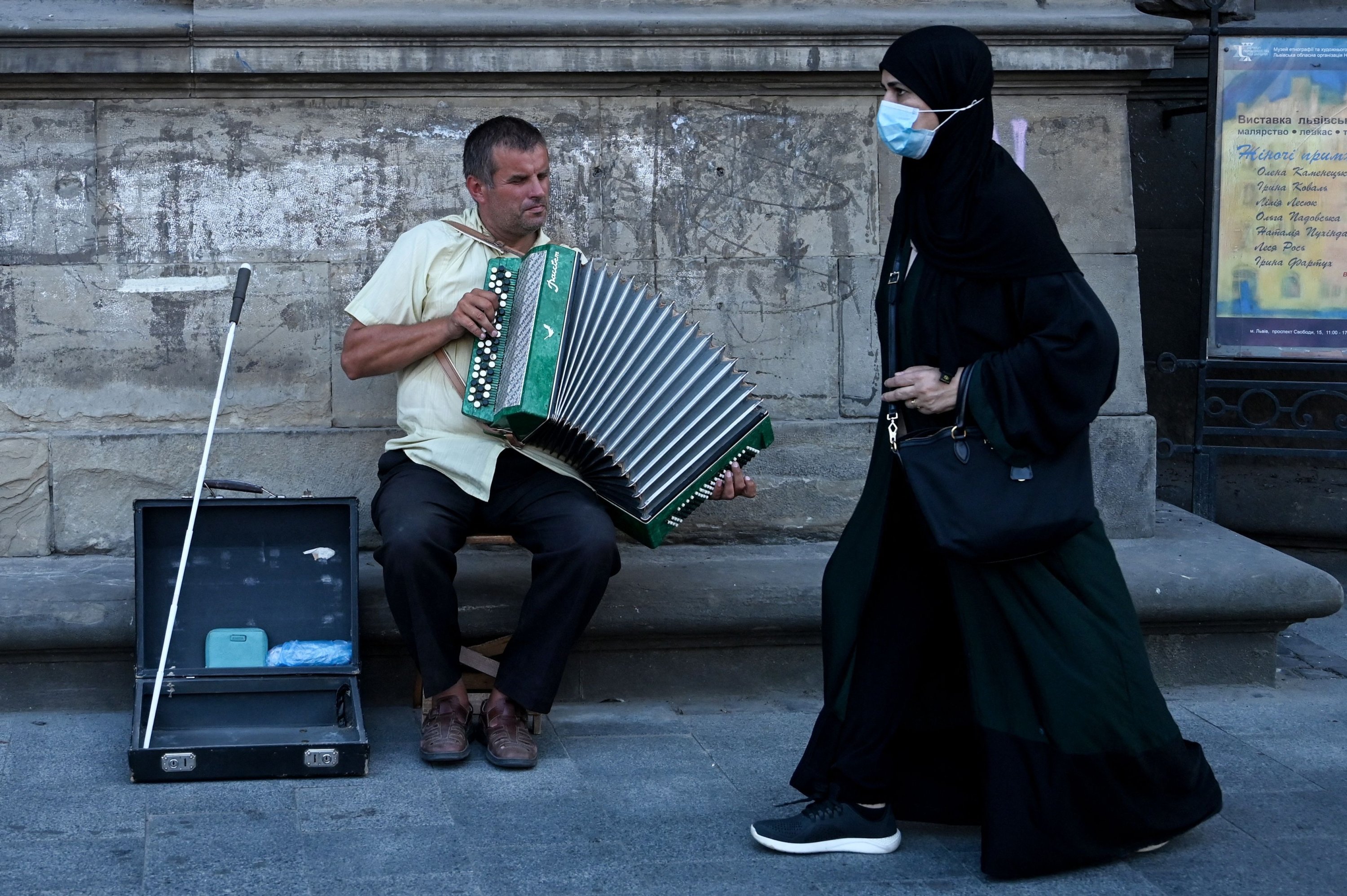 Жінка з Близького Сходу проходить повз вуличного музиканта у Львові, Україна, 14 серпня 2021 р. (AFP Photo)