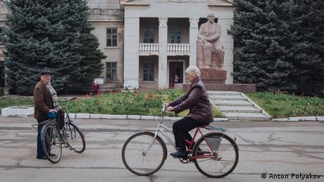 Жінка їде на велосипеді перед статуєю Леніна